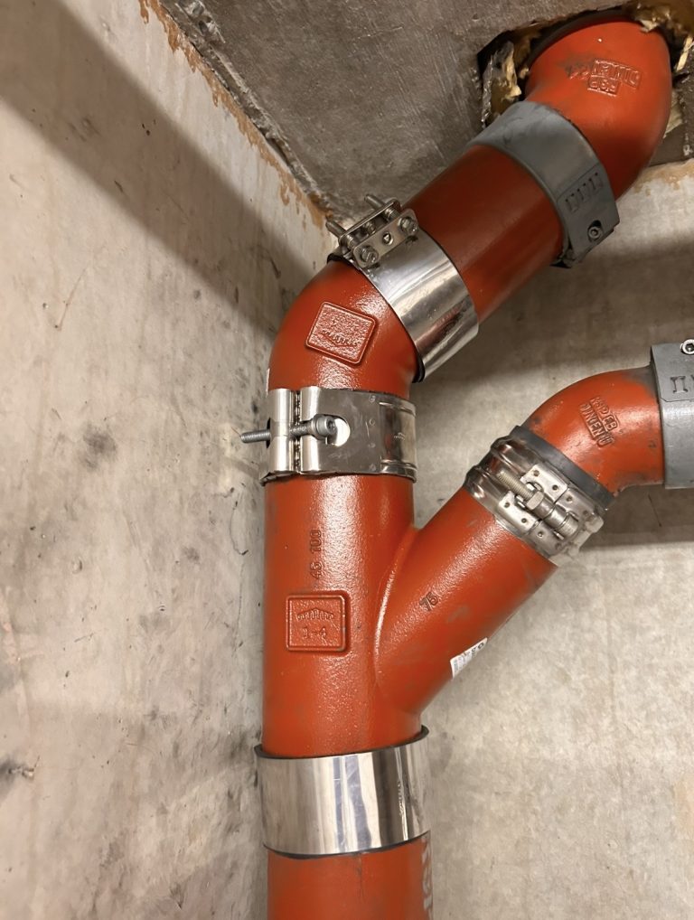 Rote Rohrverbindungen mit Metallmanschetten an einer Wand